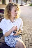 a beautiful middle age woman in 70s, 80s style clothes is looking at her smartphone on a bench photo