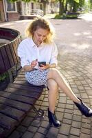 a beautiful middle age woman in 70s, 80s style clothes is looking at her smartphone on a bench photo