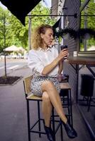 a beautiful middle age woman in 70s, 80s style clothes drinks coffee sitting at the bar in a modern cafe photo