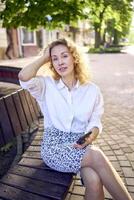 a beautiful middle age woman in 70s, 80s style clothes is looking at her smartphone on a bench photo