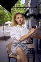 a beautiful middle age woman in 70s, 80s style clothes drinks coffee sitting at the bar in a modern cafe photo
