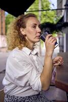 a beautiful middle age woman in 70s, 80s style clothes drinks coffee sitting at the bar in a modern cafe photo