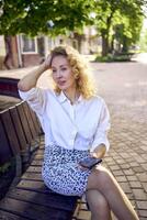 a beautiful middle age woman in 70s, 80s style clothes is looking at her smartphone on a bench photo