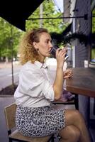 a beautiful middle age woman in 70s, 80s style clothes drinks coffee sitting at the bar in a modern cafe photo