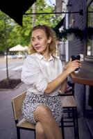 a beautiful middle age woman in 70s, 80s style clothes drinks coffee sitting at the bar in a modern cafe photo