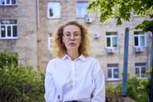 middle age woman in 70s, 80s style clothes with a coffee stain on her blouse in front of gray houses of the 70s photo