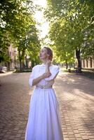 chic middle age woman in a white vintage dress in a sunlit alley photo