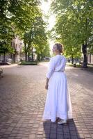 chic middle age woman in a white vintage dress in a sunlit alley photo