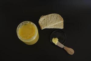 mantequilla ghee en un transparente tarro con hecho en casa un pan en un negro antecedentes foto