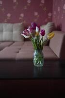 bouquet of multicolored tulips in a transparent jar in the interior photo