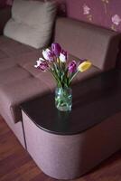 bouquet of multicolored tulips in a transparent jar in the interior photo