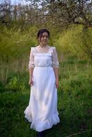 beautiful woman in white vintage dress with train in spring garden at sunset photo