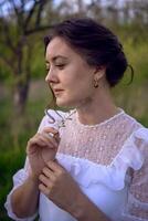 beautiful woman in white vintage dress with train in spring garden at sunset photo