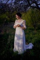 beautiful woman in white vintage dress with train in spring garden at sunset photo