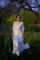 beautiful woman in white vintage dress with train in spring garden at sunset photo