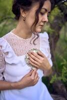 beautiful woman in white vintage dress with train and holding vintage mirror in spring garden at sunset photo