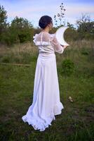 un hermosa mujer en un blanco Clásico vestir con un tren sostiene un espejo en el forma de el Luna foto