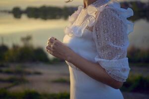 a woman in a white vintage dress on the shore of a lake at sunset photo