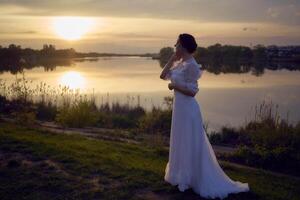 a woman in a white vintage dress on the shore of a lake at sunset photo