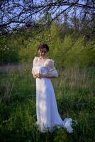 beautiful woman in white vintage dress with train in spring garden at sunset photo