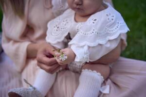 un bebé niña sostiene un flor en su manos en su de la madre brazos foto