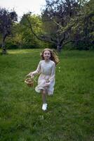 un pequeño niña con largo pelo carreras mediante el jardín con un cesta lleno de flores foto