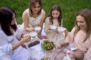 two women and their children having a picnic on the lawn photo