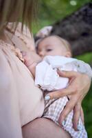 beautiful mother is breastfeeding her baby girl in the garden photo