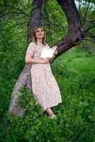 woman in a pastel dress reads a book near a tree in the garden, mockup photo