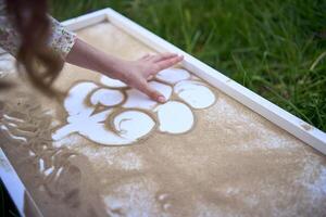 a cute girl in a pastel dress draws with sand on a special table photo