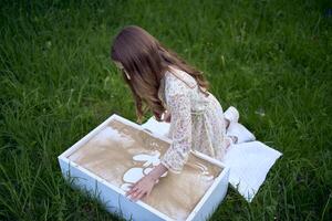 a cute girl in a pastel dress draws with sand on a special table photo