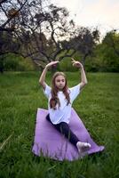 the girl is sitting in twine on a yoga mat in the garden photo