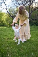 a baby girl walks holding her mother's hands in the park photo