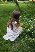 un pequeño niña con largo pelo recoge flores en un Pascua de Resurrección cesta foto