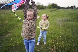 dos pequeño hermanas y madre correr y lanzamiento un cometa en un campo foto