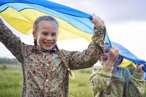 dos pequeño muchachas en el campo debajo el ucranio bandera en lluvia foto