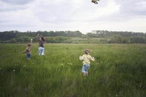 two little sisters and mother run and launch a kite in a field photo