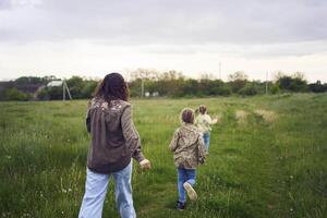 mother and children run holding hands in the field photo