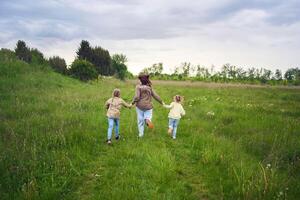 mother and children run holding hands in the field photo