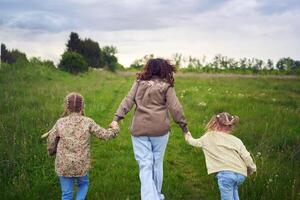 mother and children run holding hands in the field photo