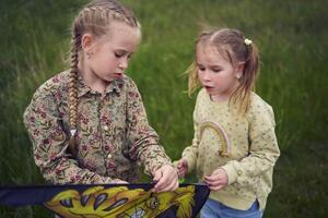 two little sisters repair and fly a kite in a field photo