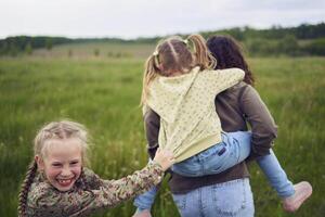 un madre rollos su hijas en su atrás, jugando caballo, Besos y abrazos foto