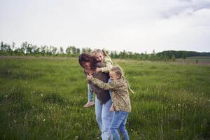 un madre rollos su hijas en su atrás, jugando caballo, Besos y abrazos foto