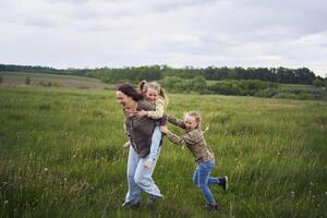 un madre rollos su hijas en su atrás, jugando caballo, Besos y abrazos foto