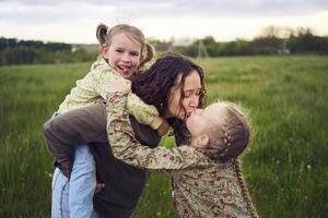 un madre rollos su hijas en su atrás, jugando caballo, Besos y abrazos foto