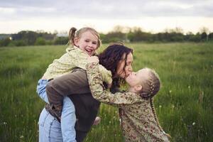 un madre rollos su hijas en su atrás, jugando caballo, Besos y abrazos foto