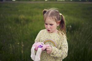 un hermosa rubio niña con su juguete conejito es jugando en el campo foto