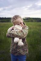 un hermosa rubio niña con su juguete conejito es jugando en el campo foto