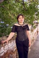 a medium size woman in a black corset and wide leg trousers walks through the city in the morning light photo