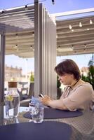 plus size woman in peach fuzz dress chooses a dish in a restaurant via QR code in smartphone, water with lemon and glasses in front of her photo